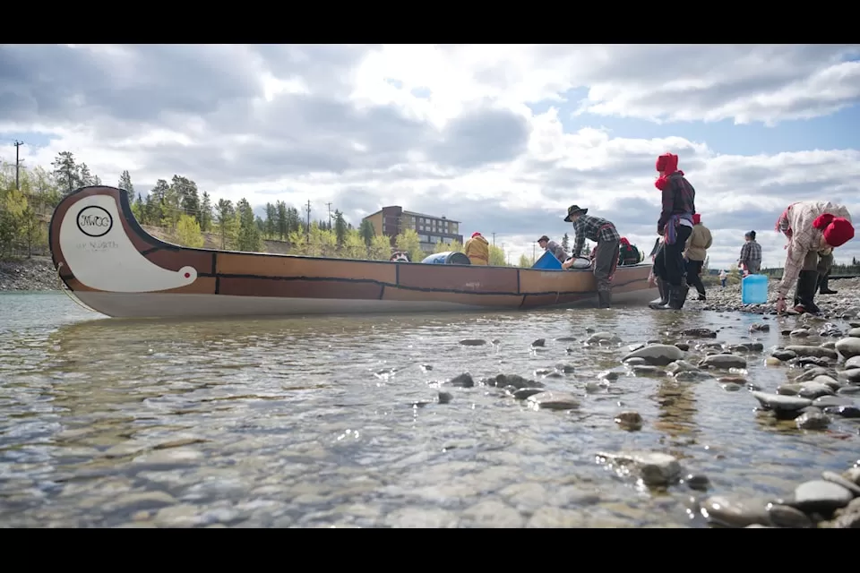 Grade 9 students dressed in historical clothing pack supplies into a large canoe for a voyageur simulation trip on the Yukon River.