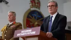 UK Defence officials including the Defence Secretary speaking at a podium, likely addressing the agreement to transfer Chagos Islands sovereignty and its implications for the Diego Garcia military base.