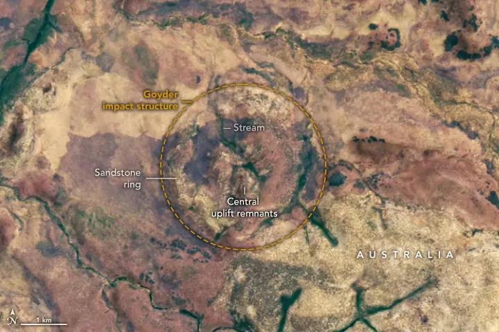 Satellite image showing the subtle circular pattern of the eroded Goyder impact structure in Australia's Northern Territory, highlighting remnants of the central uplift as hills and a sandstone ring within dry savanna landscape.