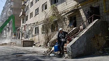 Elderly woman carrying belongings from a damaged Kyiv apartment building after a Russian missile attack