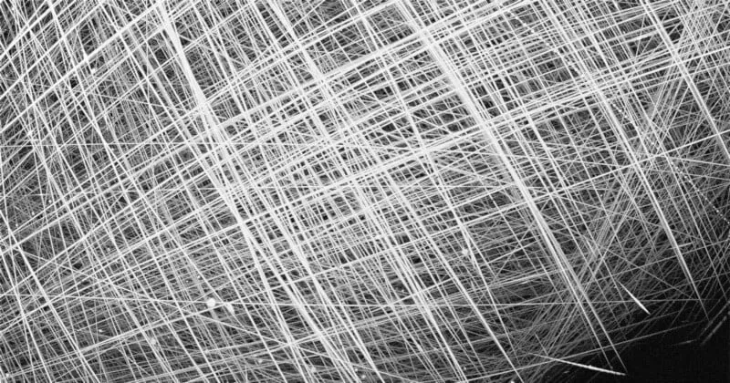 White streaks crisscrossing a dark sky, showing the paths of multiple satellites captured over the Arctic in a single image.