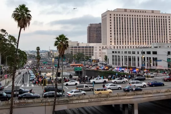 Downtown Los Angeles cityscape with signs of protest activity or police presence visible in the distance