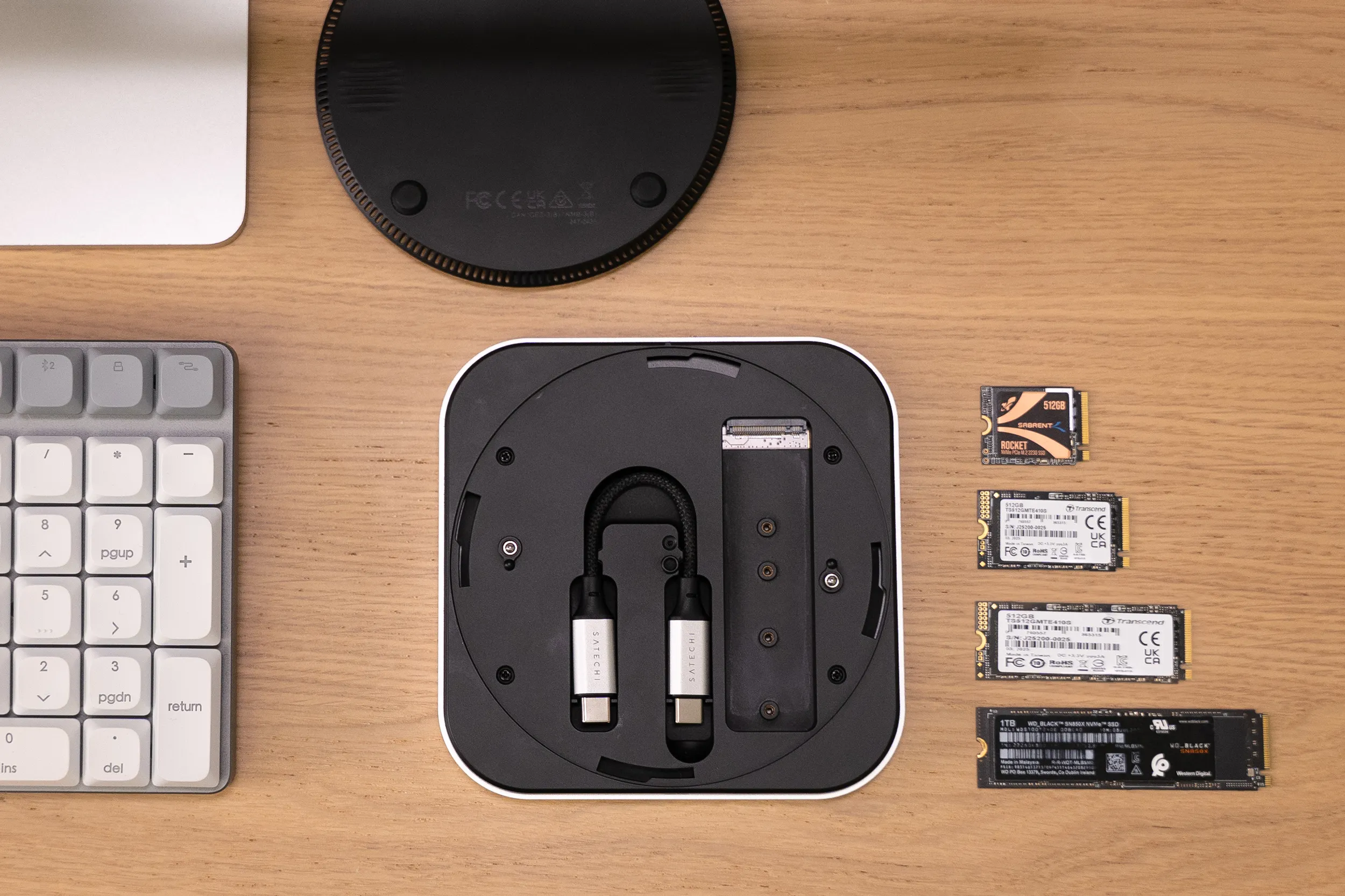 Satechi's new USB4 NVMe SSD enclosure shown upside down on a wooden desk, alongside several bare NVMe solid-state drives, highlighting its compact design and storage compatibility.