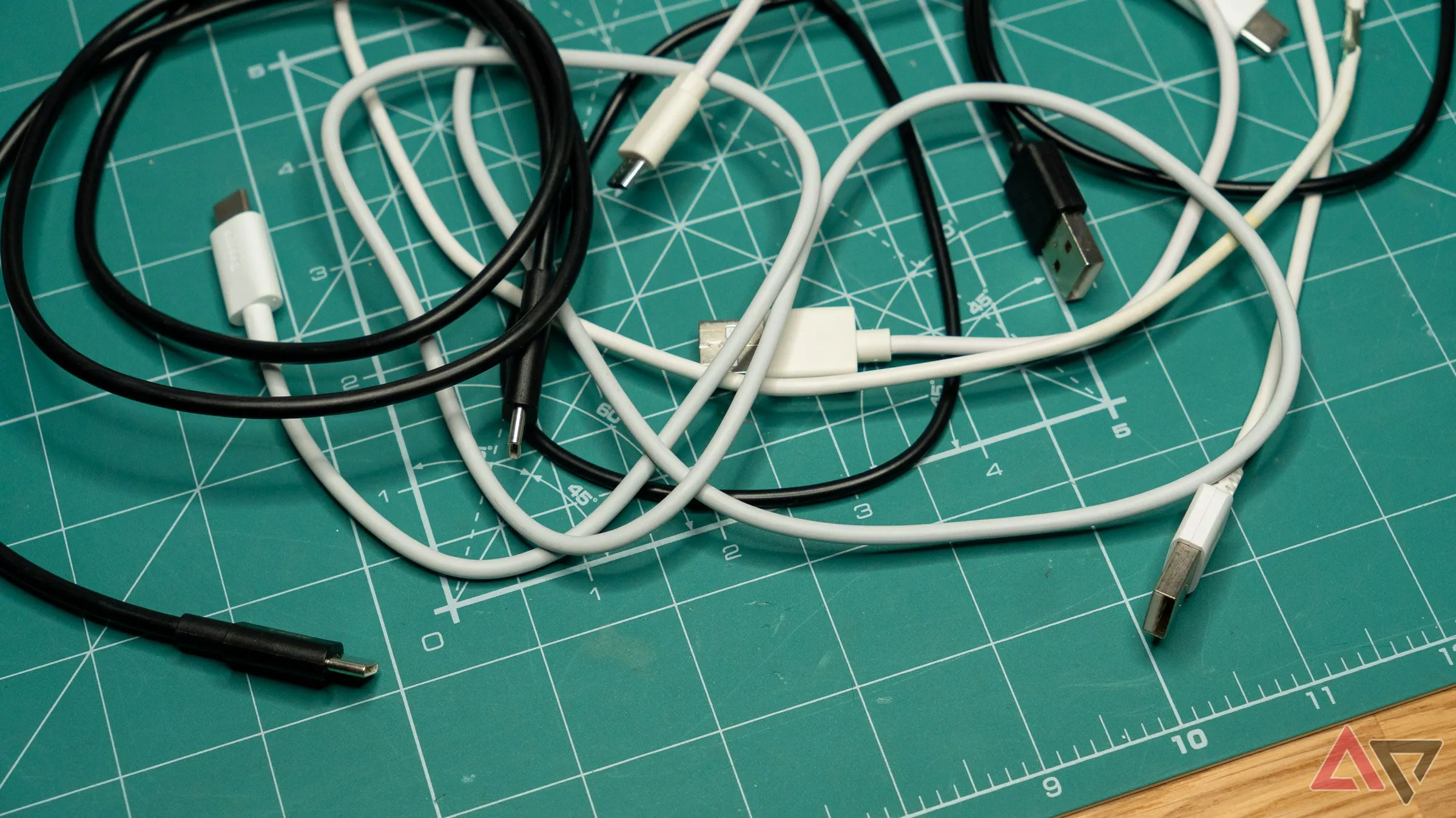 Black and white USB-C and other charging cables scattered on a green mat, illustrating different types of cables.