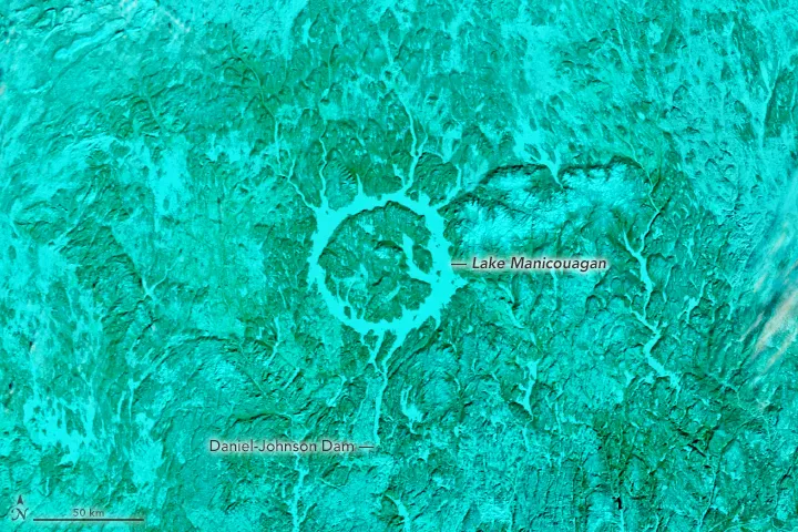 False-color satellite image highlights the ring lake and surrounding snowy terrain in shades of blue, while vegetation appears greenish-blue.
